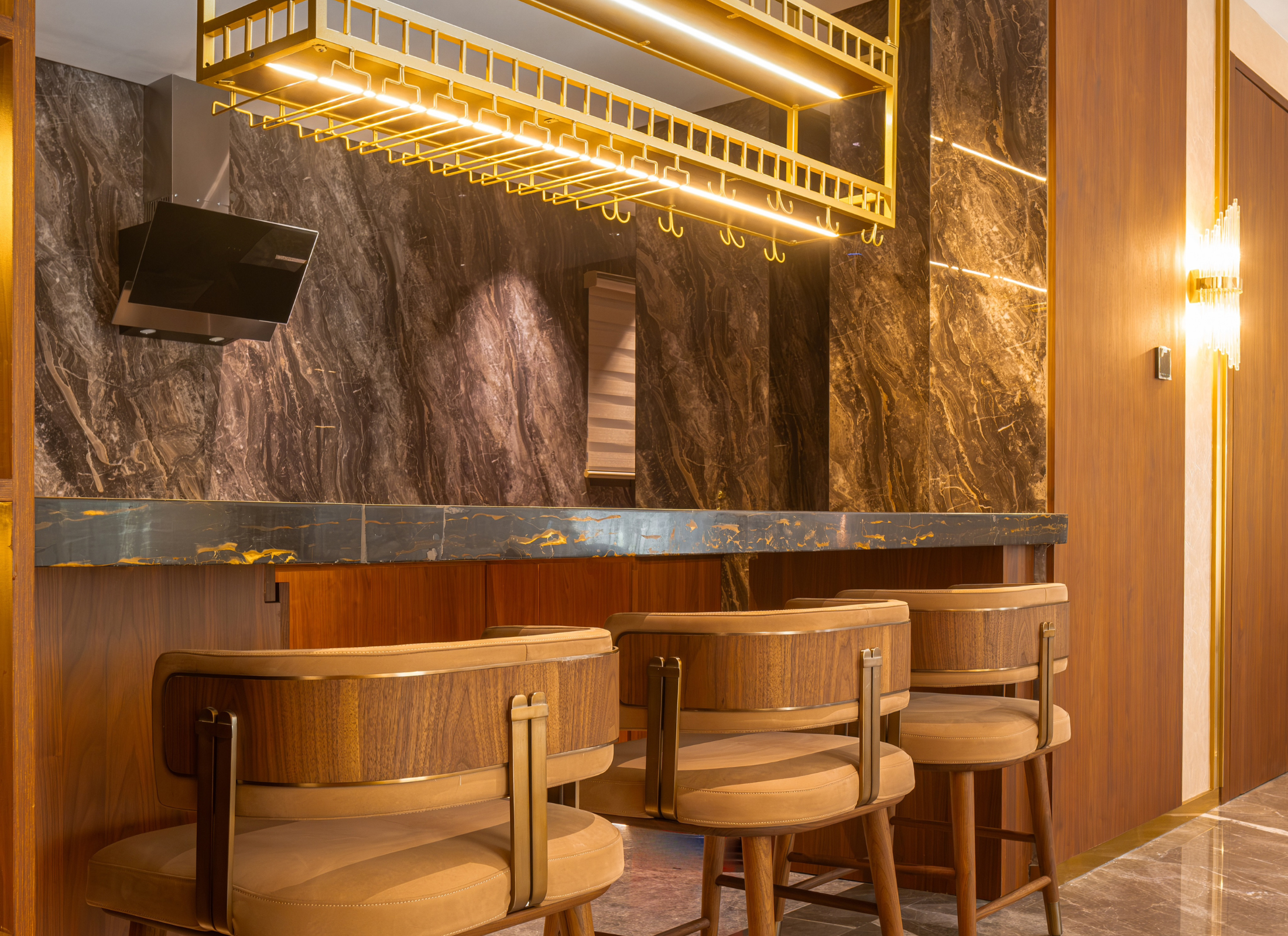 Modern bar interior with marble wall, wooden bar stools, and decorative lighting.