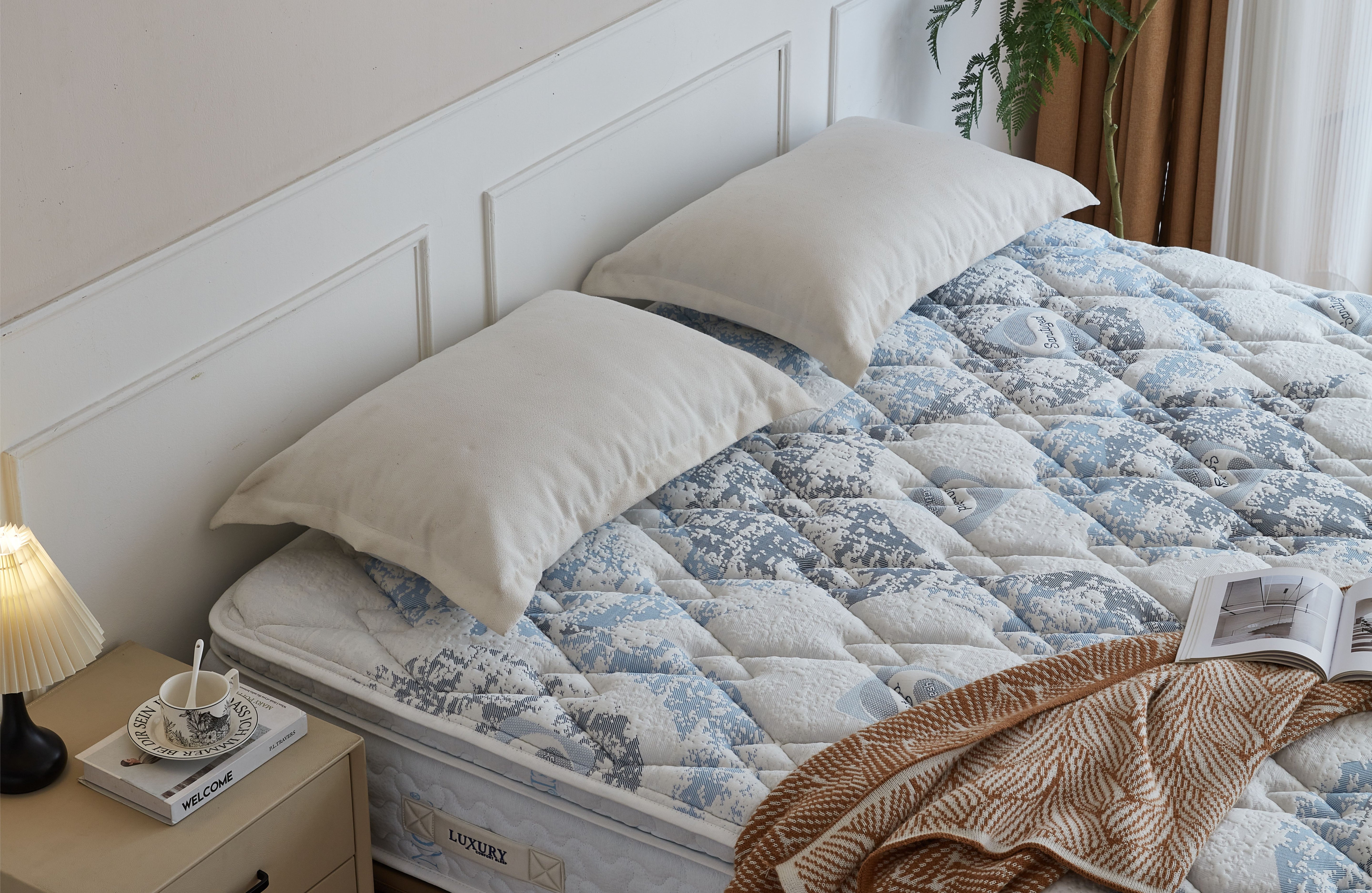Bed with floral quilt, pillows, and a side table with a lamp and books.