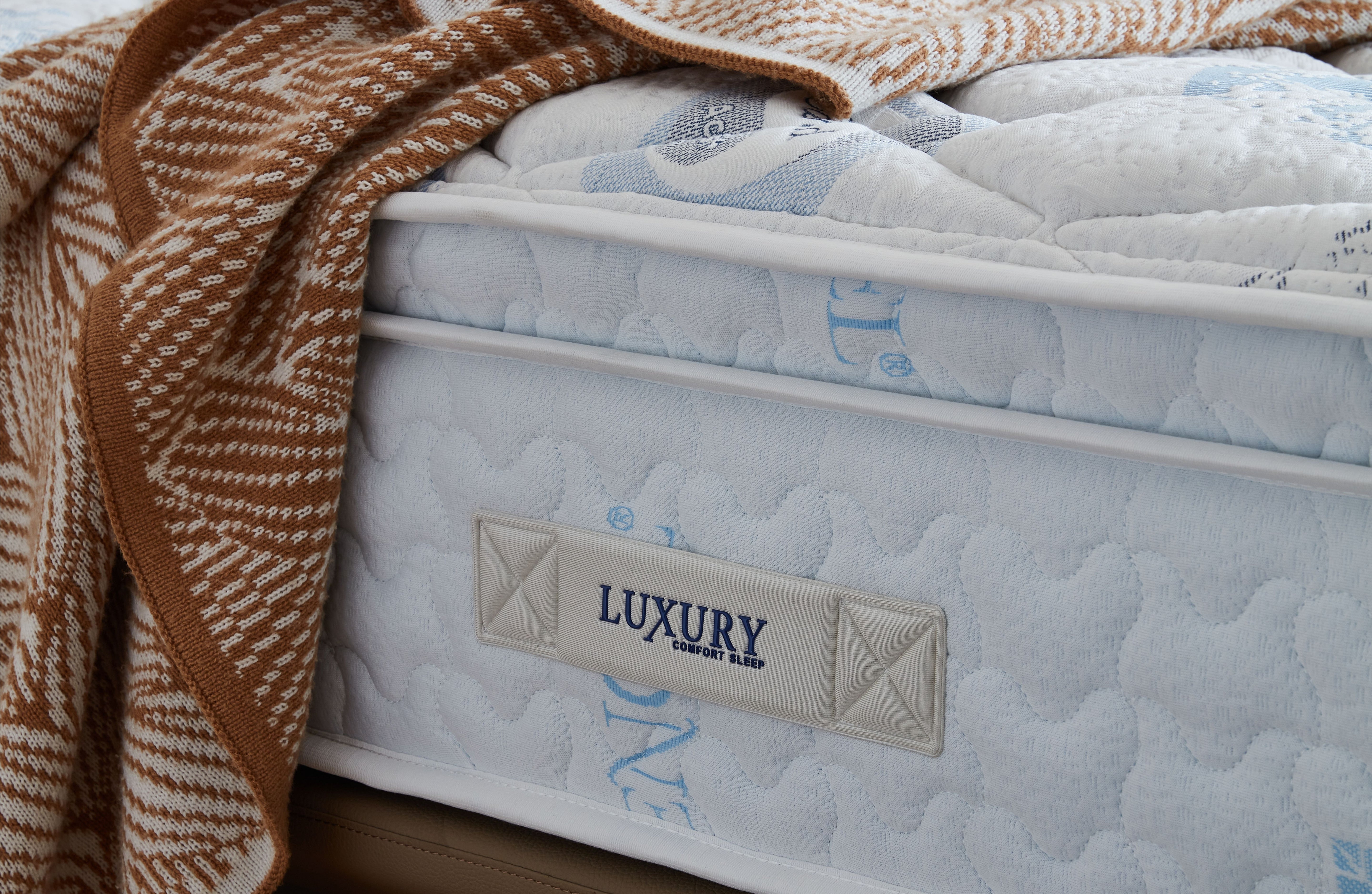 Mattress with a blanket draped over it, featuring a 'Luxury' brand label.