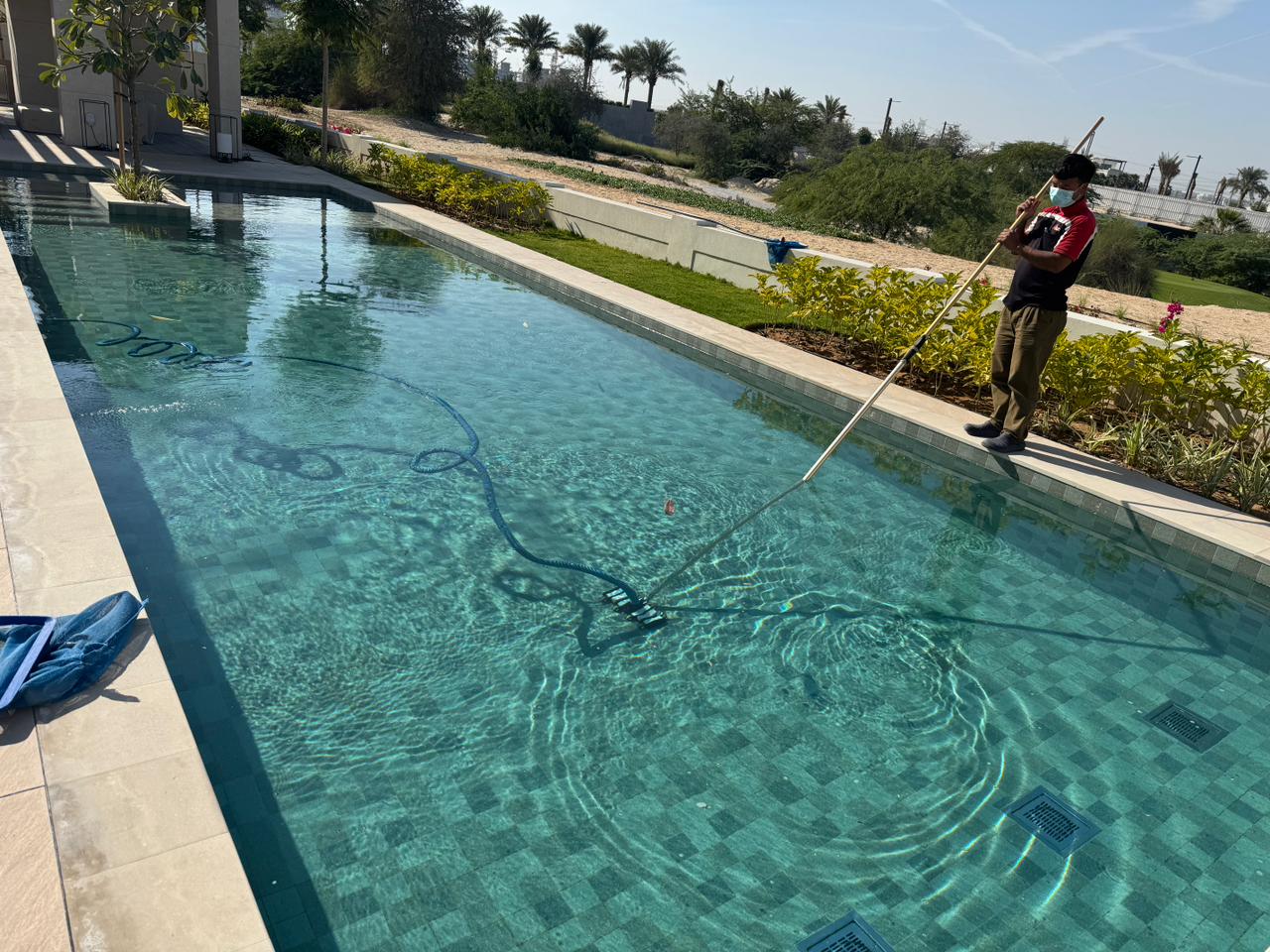 Person cleaning a pool with a long-handled brush on a sunny day.